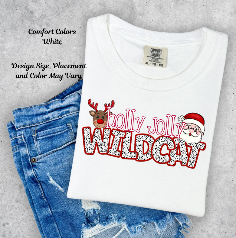 A folded white Comfort Colors t-shirt with a 'Holly Jolly Wildcat' Christmas graphic, styled on top of blue denim jeans against a textured gray concrete background.