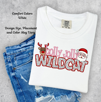 A folded white Comfort Colors t-shirt with a 'Holly Jolly Wildcat' Christmas graphic, styled on top of blue denim jeans against a textured gray concrete background.